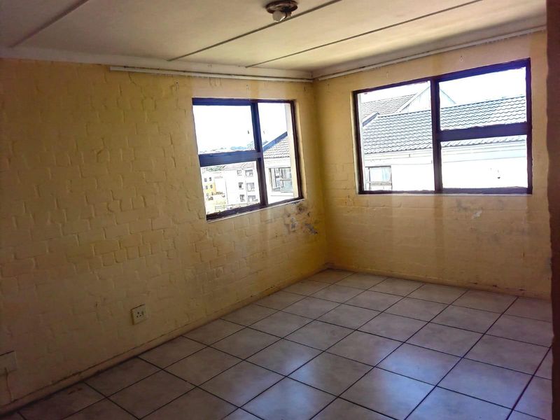 An empty bedroom featuring tiled flooring, painted brick walls, and large windows providing natural light and views of the surrounding neighborhood.