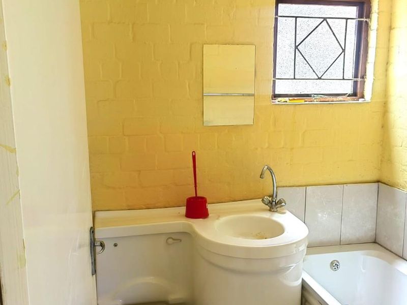 Compact bathroom featuring a combined toilet and vanity unit, a standard bathtub, and yellow painted brick walls.