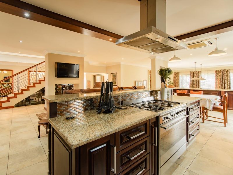 Spacious open-plan kitchen and living area featuring granite countertops, a gas cooktop, stainless steel extractor, and a modern staircase with metal railings.