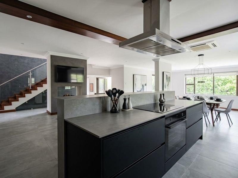 Modern open-plan living area featuring a sleek kitchen island with integrated appliances, tiled flooring, and a contemporary staircase with glass balustrades.