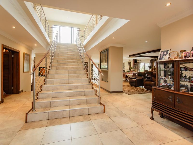 Spacious double-volume entrance hall featuring a central tiled staircase with stainless steel balustrades and recessed lighting, leading to open-plan living areas.