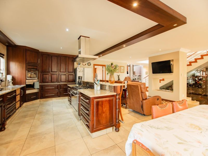 Spacious open-plan kitchen and living area featuring dark wood cabinetry, granite countertops, stainless steel appliances, and elegant wooden ceiling beams.