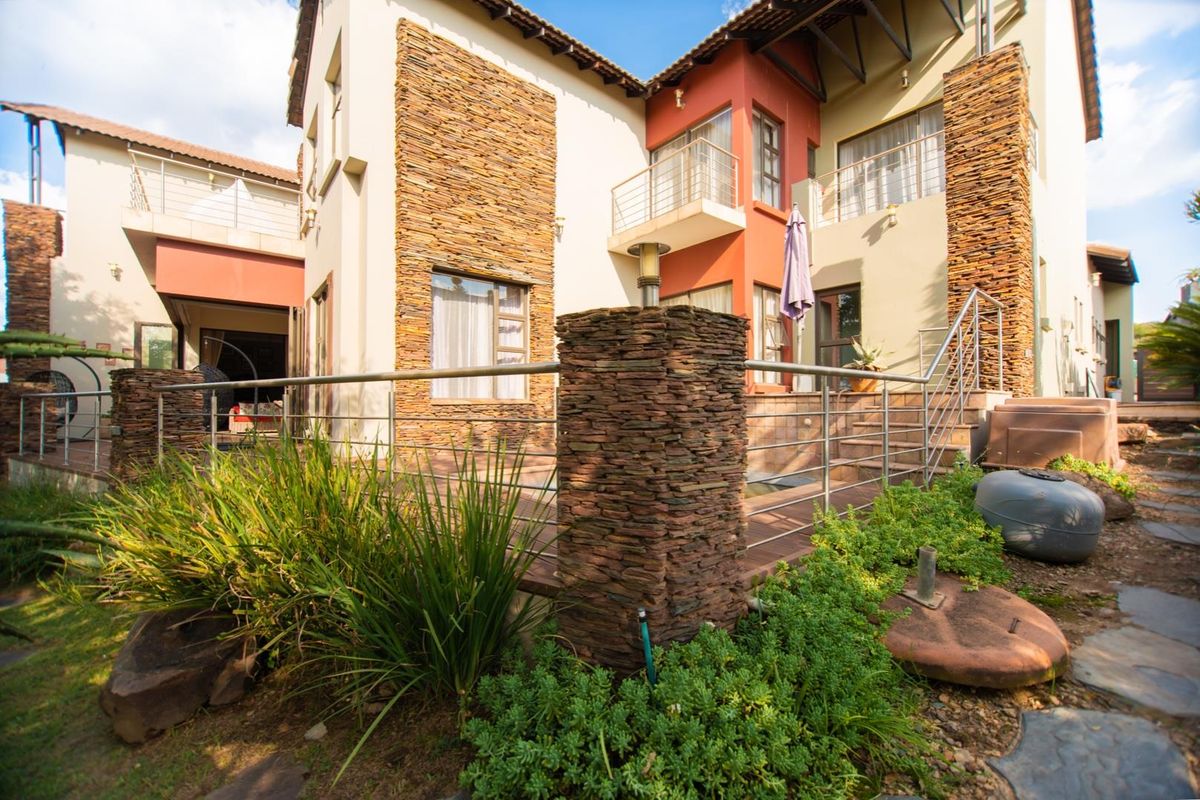 Rear elevation of a multi-story house featuring stone cladding, stainless steel balustrades, and a spacious tiled patio area.
