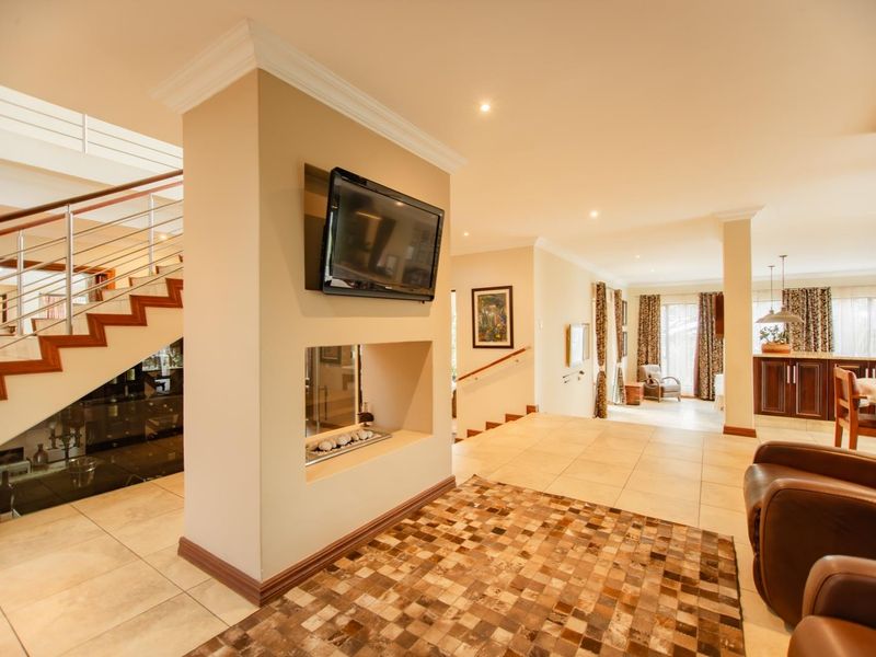 Spacious open-plan living area featuring a central built-in fireplace, tiled flooring, and a modern staircase with stainless steel balustrades.