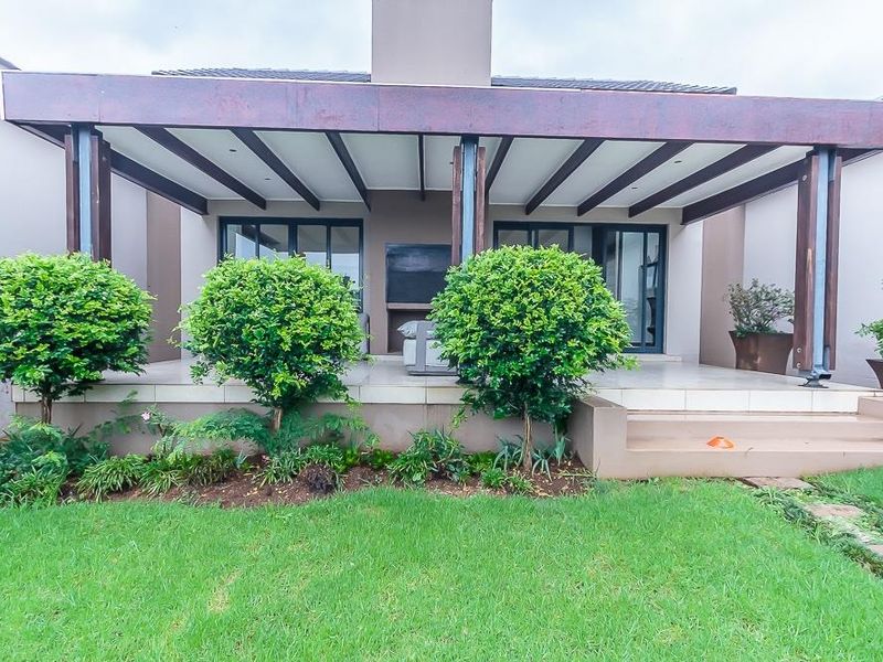 A well-maintained covered patio featuring a built-in fireplace, tiled flooring, and recessed lighting, providing a seamless transition to the rear garden.