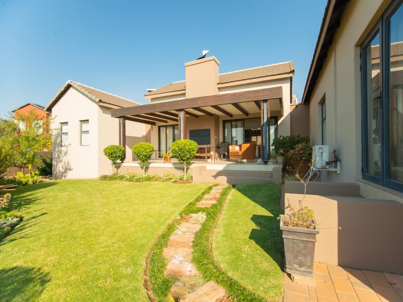 A well-maintained rear exterior featuring a covered patio with a timber pergola, built-in fireplace, and a landscaped garden with a stone pathway.