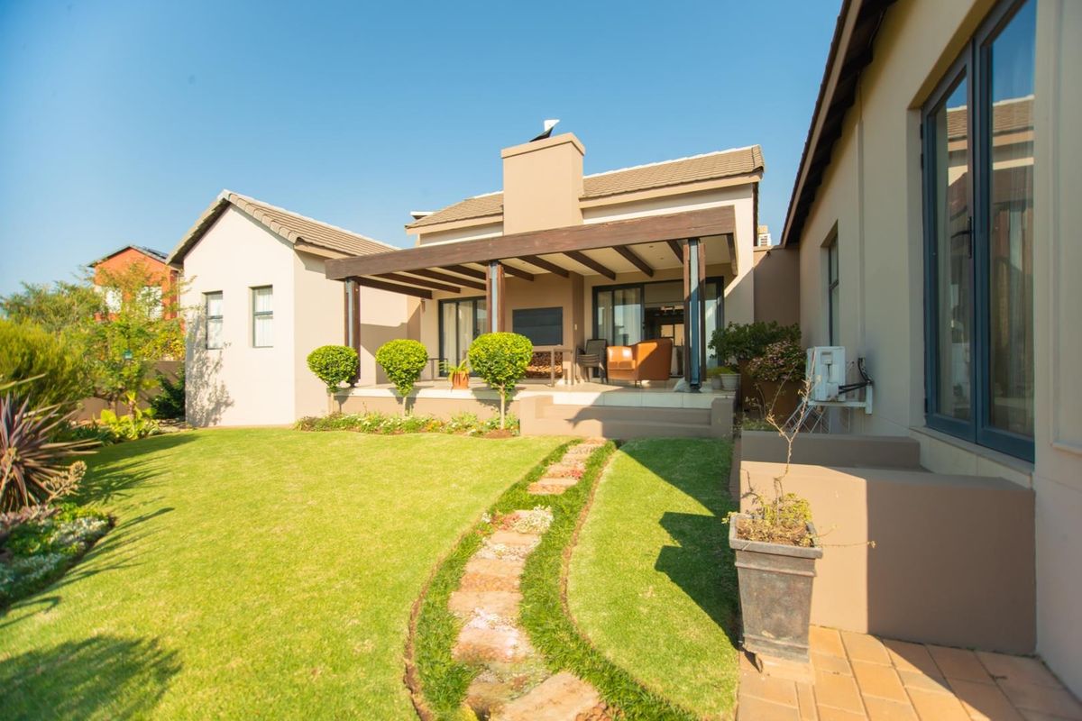 A well-maintained rear exterior featuring a covered patio with a timber pergola, built-in fireplace, and a landscaped garden with a stone pathway.