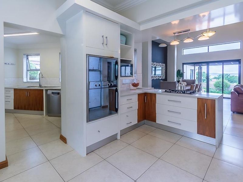 Modern open-plan kitchen featuring two-tone cabinetry, stone countertops, built-in oven, and gas cooktop, seamlessly flowing into the adjacent living and dining area.
