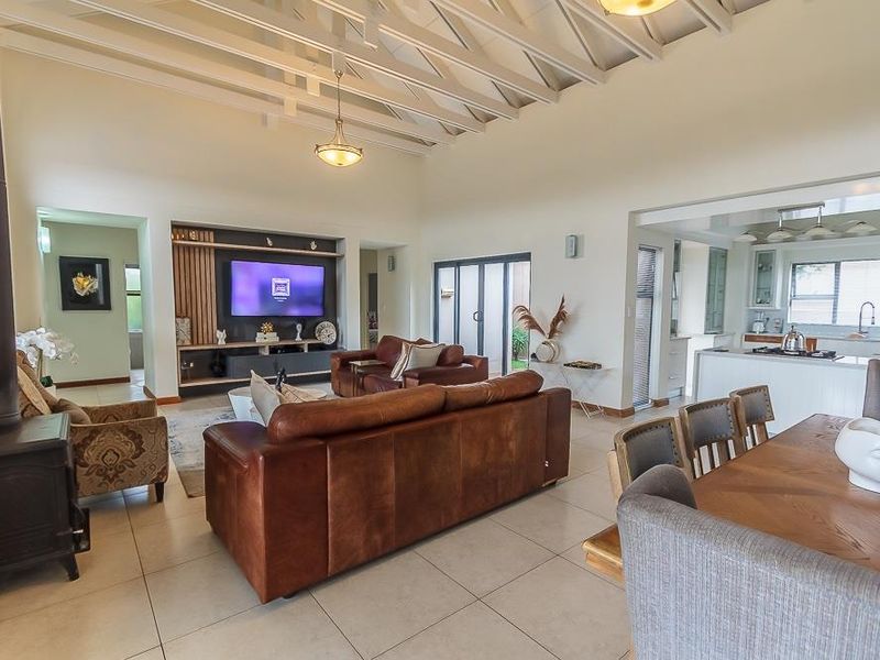 Spacious open-plan living area featuring a vaulted ceiling with exposed beams, a cozy fireplace, and a modern kitchen with a central island.
