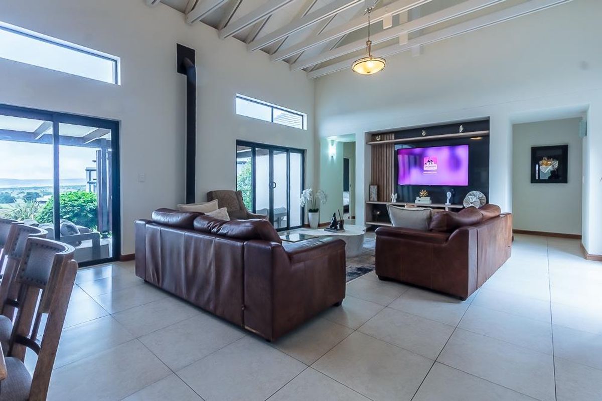Spacious living room featuring vaulted ceilings with exposed rafters, tiled flooring, a built-in media unit, and large sliding glass doors leading to the patio.