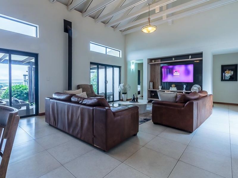 Spacious living room featuring vaulted ceilings with exposed rafters, tiled flooring, a built-in media unit, and large sliding glass doors leading to the patio.