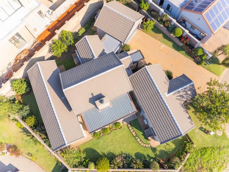 Aerial view of the property showcasing the tiled roof structure, chimney, surrounding landscaped garden, and paved driveway access.