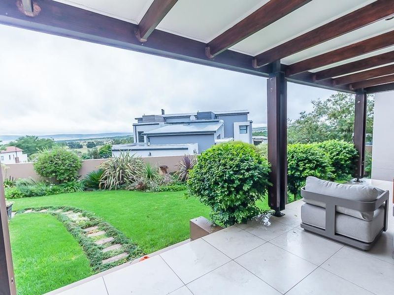 A covered patio featuring a timber pergola and tiled flooring, overlooking a well-maintained garden and surrounding landscape.