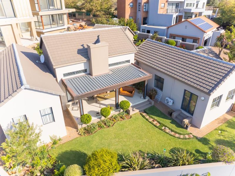 Aerial view of a residential property featuring a tiled roof, a covered patio area, and a well-maintained landscaped garden.
