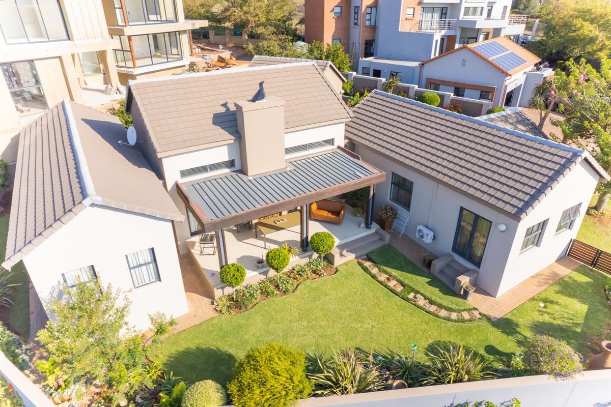 Aerial view of a residential property featuring a tiled roof, a covered patio area, and a well-maintained landscaped garden.