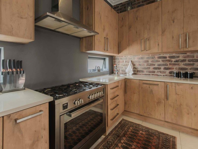 Modern kitchen featuring wood-look cabinetry, stone countertops, an exposed brick backsplash, and a stainless steel gas stove with an integrated extractor fan.