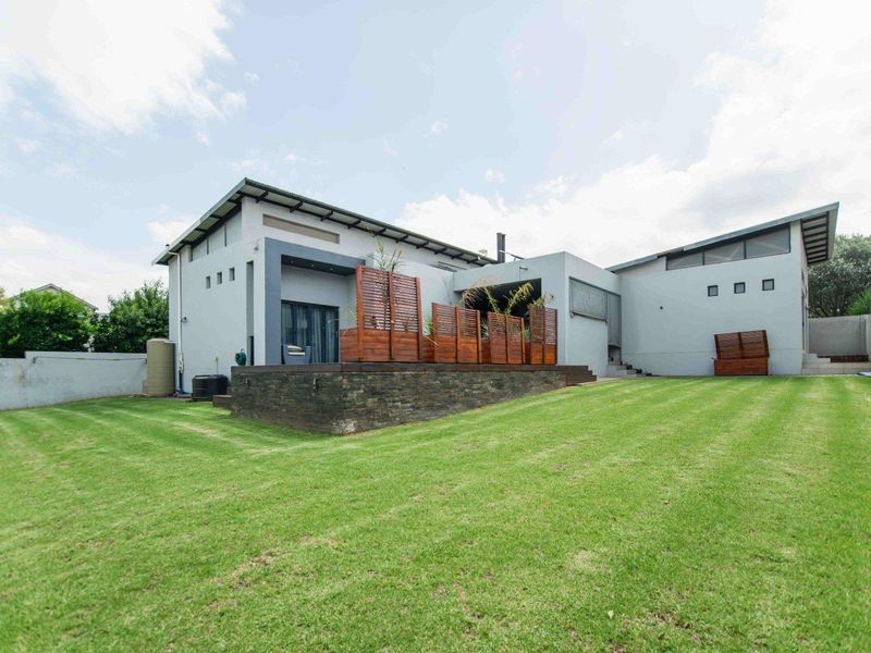 Rear view of the property featuring a spacious lawn, raised timber deck with stone cladding, and privacy screens, showcasing a modern architectural design.