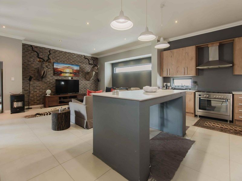 Spacious open-plan living area featuring a modern kitchen with island, built-in appliances, and a cozy lounge area with a feature brick wall and stove.