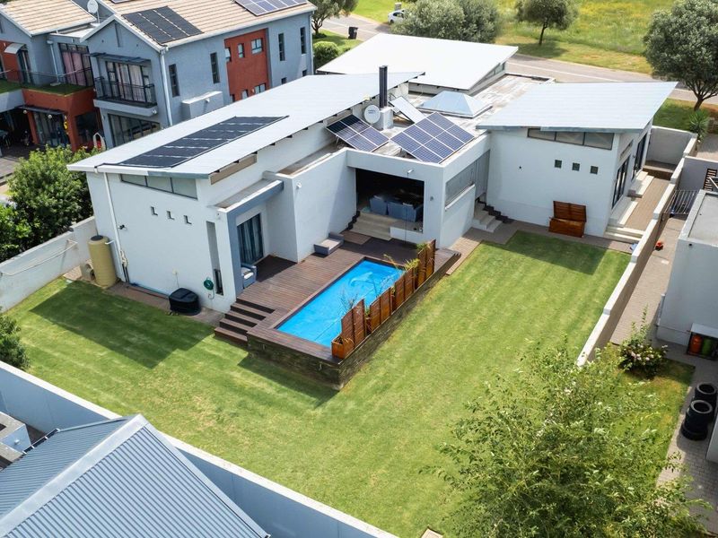 Aerial view of a modern residential property featuring a swimming pool, timber decking, landscaped lawn, and roof-mounted solar panels.