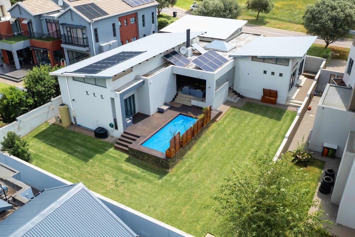 Aerial view of a modern residential property featuring a swimming pool, timber decking, landscaped lawn, and roof-mounted solar panels.