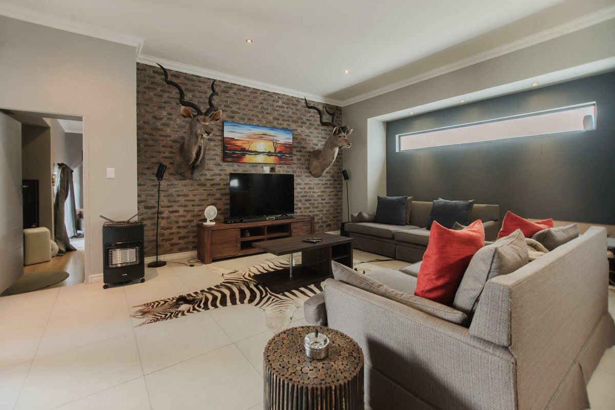Spacious living room featuring an exposed brick accent wall, recessed lighting, and modern tiled flooring with a clerestory window for natural light.