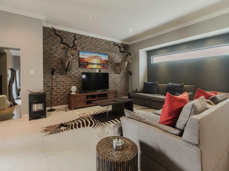 Spacious living room featuring an exposed brick accent wall, recessed lighting, and modern tiled flooring with a clerestory window for natural light.