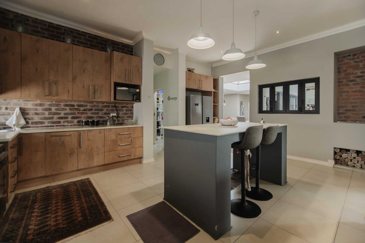 Modern kitchen featuring wood-finish cabinetry, an island with seating, exposed brick accents, and contemporary pendant lighting.