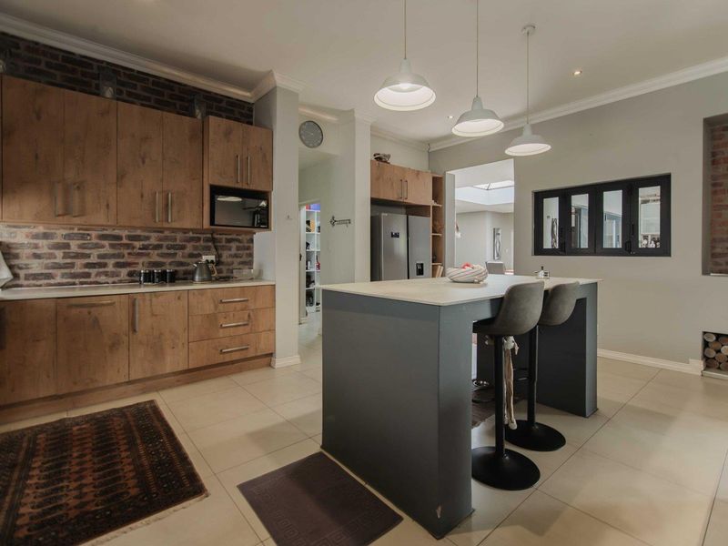 Modern kitchen featuring wood-finish cabinetry, an island with seating, exposed brick accents, and contemporary pendant lighting.