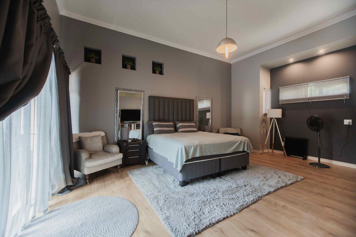 Spacious bedroom featuring neutral grey walls, laminate flooring, recessed wall niches, and elegant pendant lighting, creating a comfortable and modern living space.