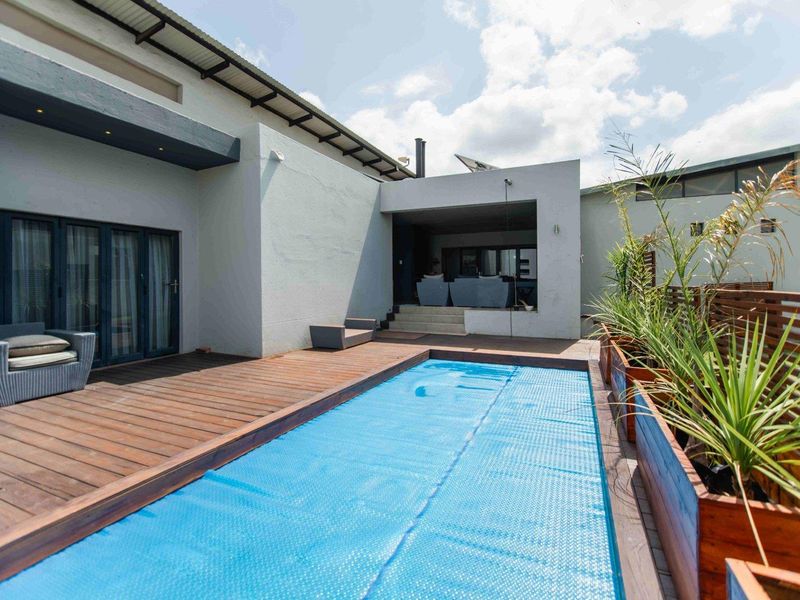 A well-maintained outdoor pool area featuring wooden decking, a swimming pool with a cover, and modern architectural finishes.