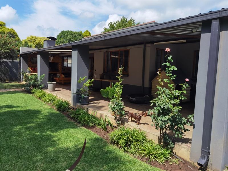 A spacious covered patio featuring a built-in braai area, overlooking a well-maintained garden with established landscaping.