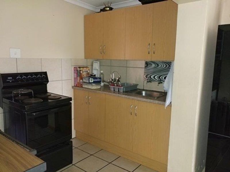 A functional kitchen featuring laminate cabinetry, a stainless steel sink, tiled backsplash, and a freestanding electric stove with ceramic floor tiles.
