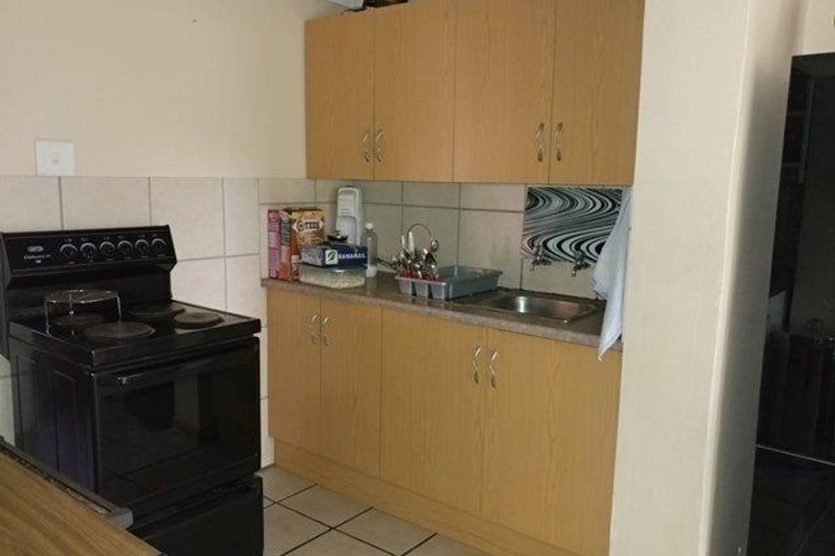 A functional kitchen featuring laminate cabinetry, a stainless steel sink, tiled backsplash, and a freestanding electric stove with ceramic floor tiles.