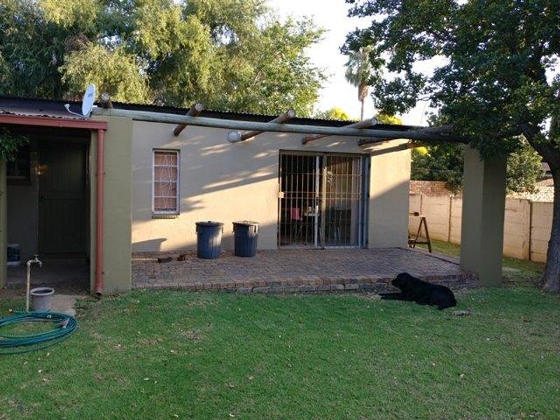 A rear patio area featuring brick paving, a timber beam pergola structure, and a sliding glass door with security gate access.