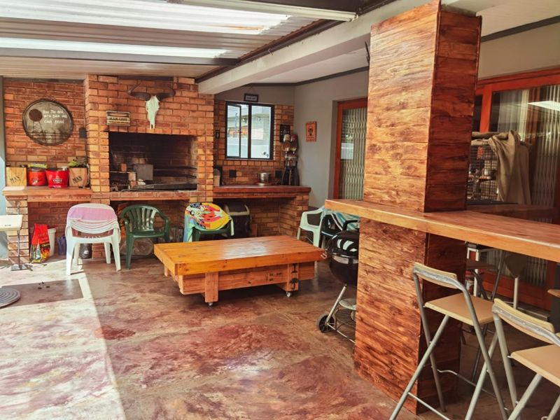 Covered outdoor patio featuring a built-in brick braai, brick prep counter, and a wooden bar area, ideal for outdoor entertaining.