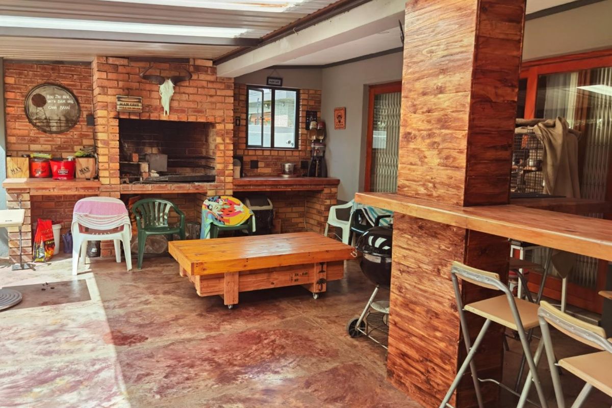 Covered outdoor patio featuring a built-in brick braai, brick prep counter, and a wooden bar area, ideal for outdoor entertaining.