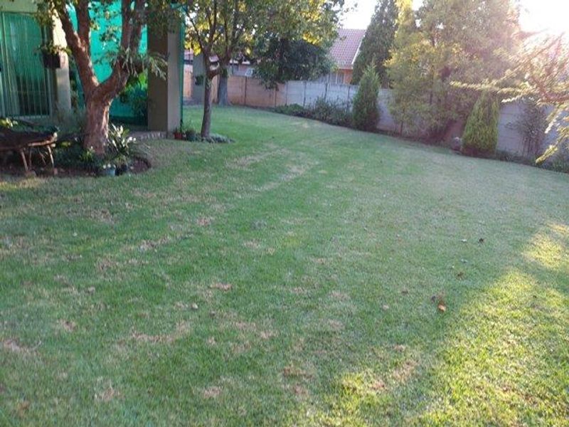 A spacious private garden featuring a large lawn area, mature trees, and a secure perimeter wall.