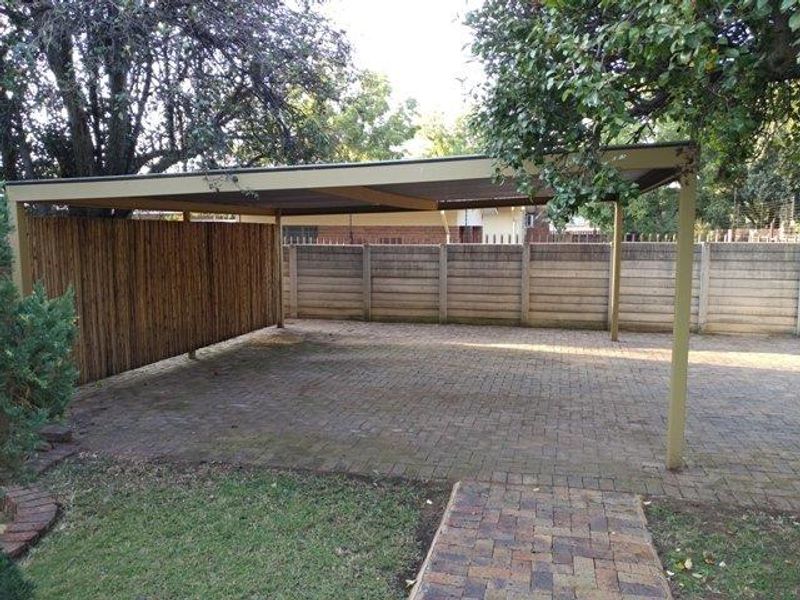 A spacious outdoor carport featuring a paved driveway, covered parking structure, and secure perimeter walling.