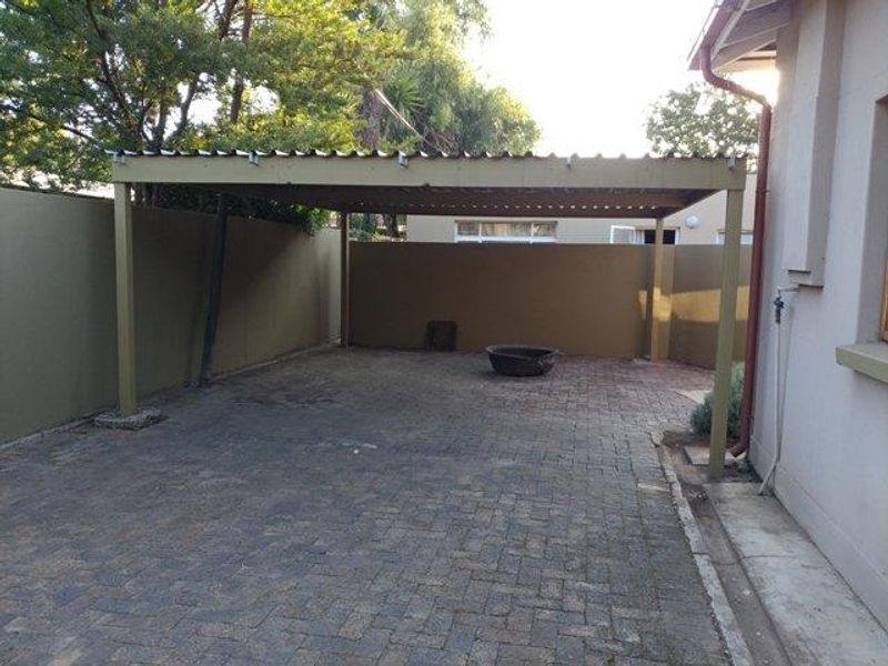 A covered outdoor patio area featuring paved flooring and boundary walls, providing a functional space for outdoor living or vehicle shelter.