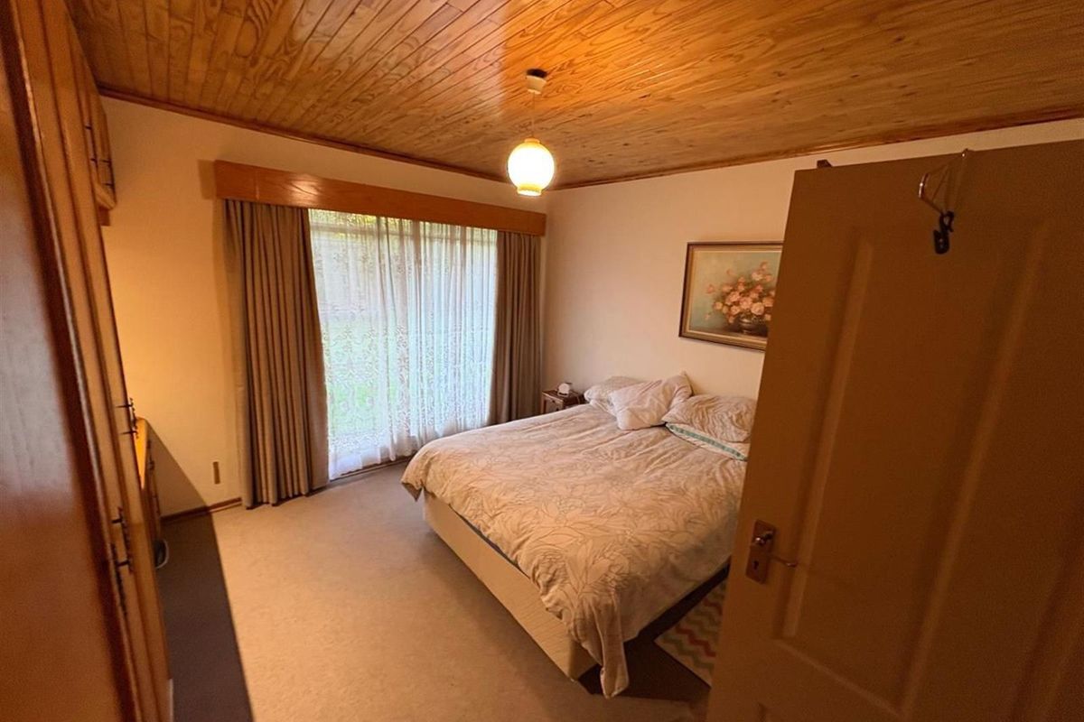 A bedroom featuring a wood-paneled ceiling, built-in cabinetry, and large windows with curtains, offering a functional and traditional living space.