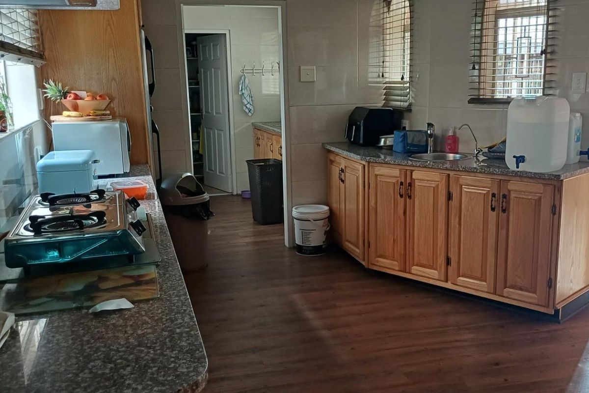 A functional kitchen featuring wood-finish cabinetry, granite-look countertops, tiled splashbacks, and an adjoining scullery area with direct access to the exterior.