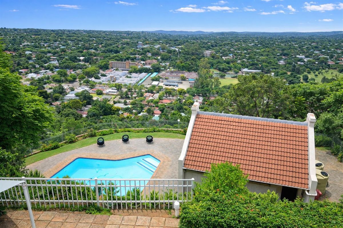 Elevated aerial view of the property featuring a swimming pool, paved patio area, and a tiled roof structure overlooking the surrounding suburban landscape.