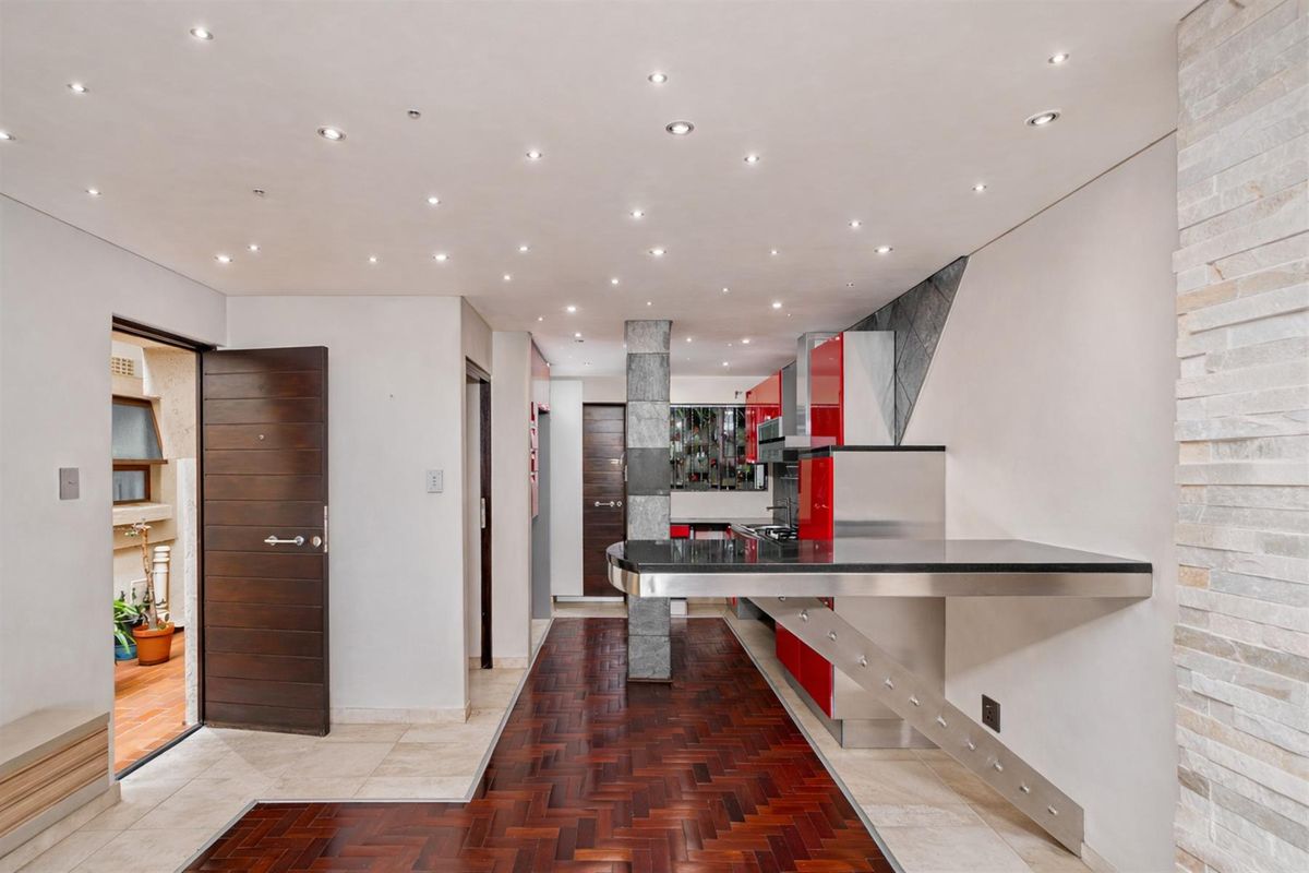 Modern kitchen featuring high-gloss red cabinetry, integrated stainless steel appliances, a sleek breakfast bar, and recessed ceiling lighting with a herringbone wood floor.