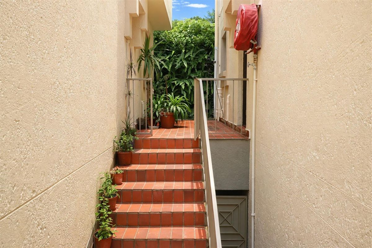 An exterior staircase with terracotta tiling leading to a rear garden area, featuring metal handrails and a wall-mounted fire hose reel.