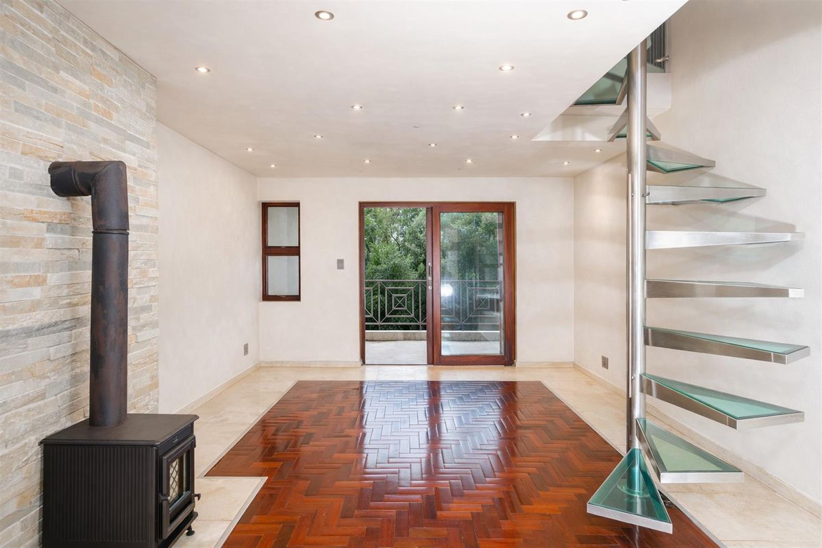 Open plan living area featuring a wood-burning stove, herringbone timber flooring, recessed lighting, and a modern glass and steel spiral staircase leading upstairs.