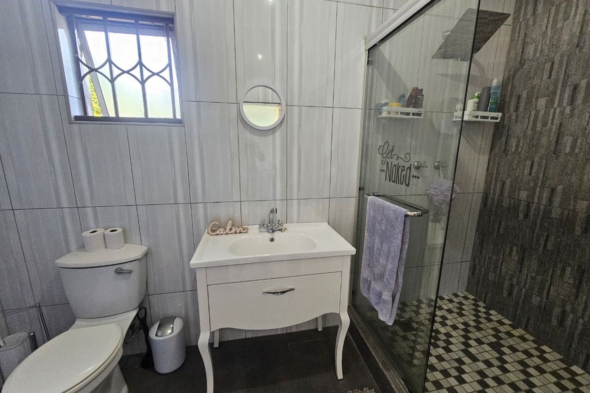 A modern bathroom featuring a vanity basin, a toilet, and a glass-enclosed shower with tiled walls and flooring.