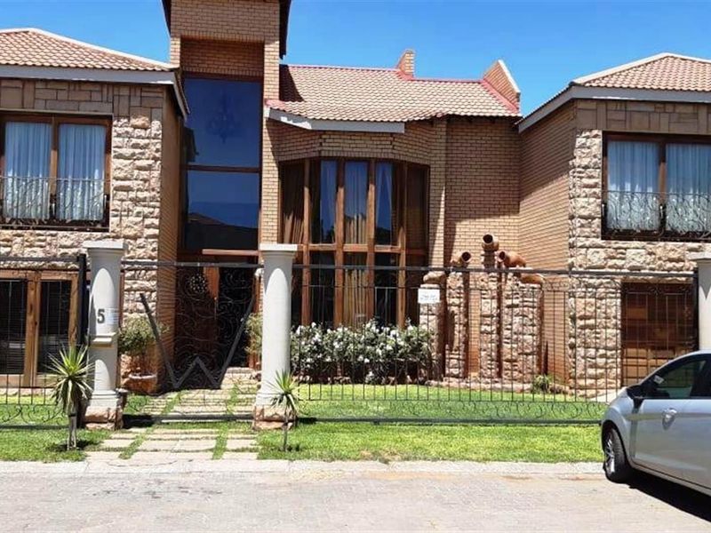 Front elevation of a multi-story residential property featuring stone and brick cladding, large windows, and a secure gated entrance.