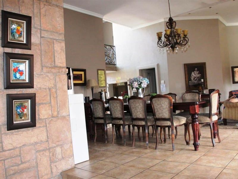 Spacious dining area featuring tiled flooring, a decorative stone-clad feature wall, and a classic chandelier, flowing into an open-plan living space.