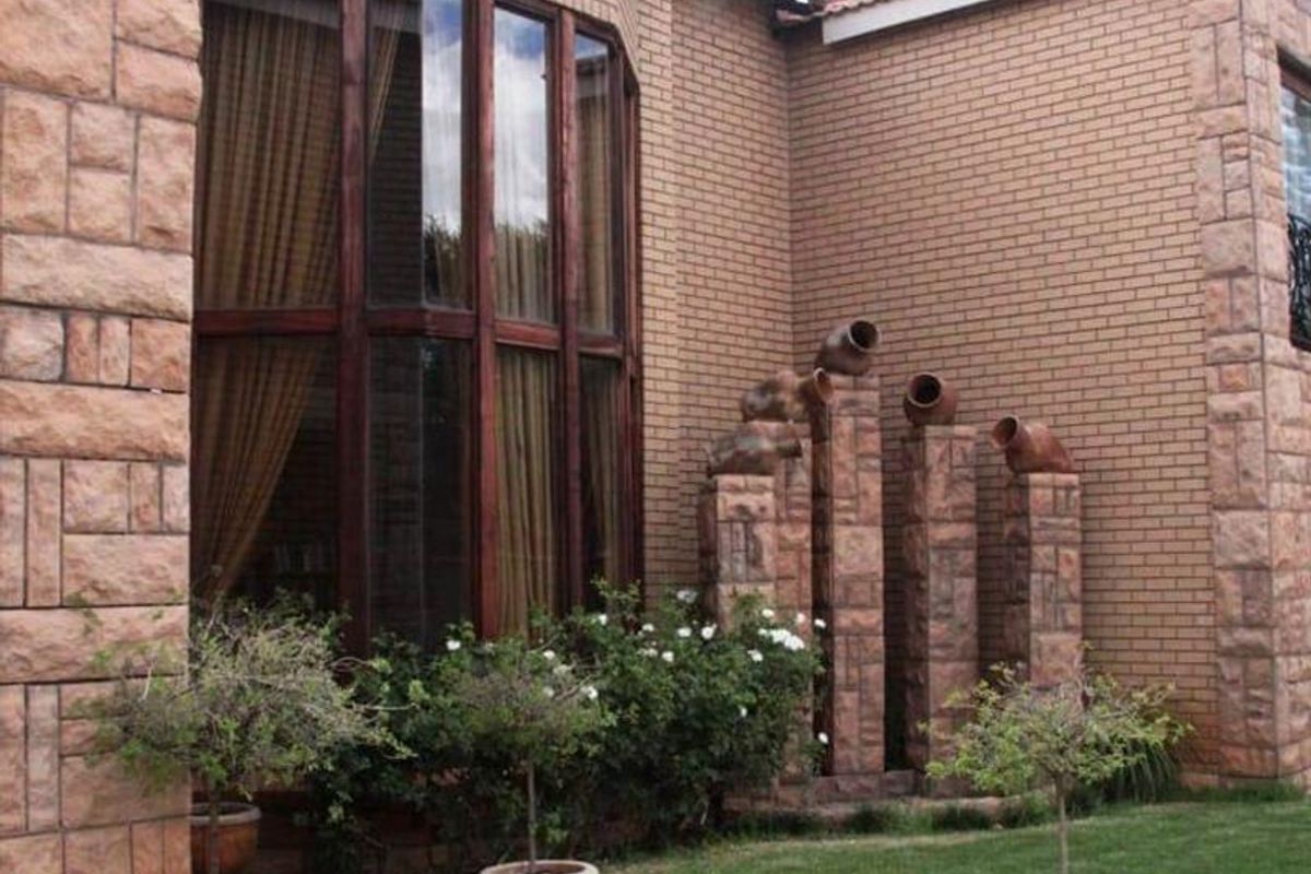 A view of the rear exterior facade featuring brick masonry, a large bay window, and a decorative stone water feature in the garden.