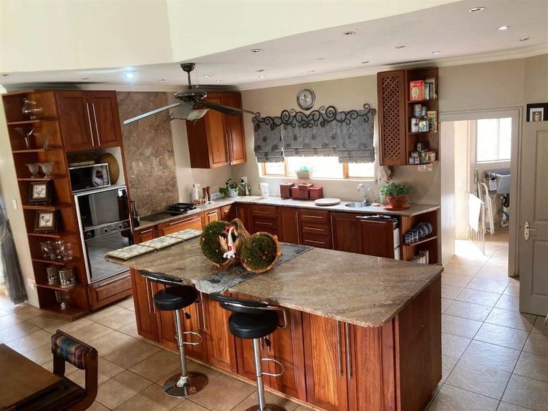 Spacious kitchen featuring wooden cabinetry, granite countertops, a central island with breakfast bar seating, and integrated oven and hob.